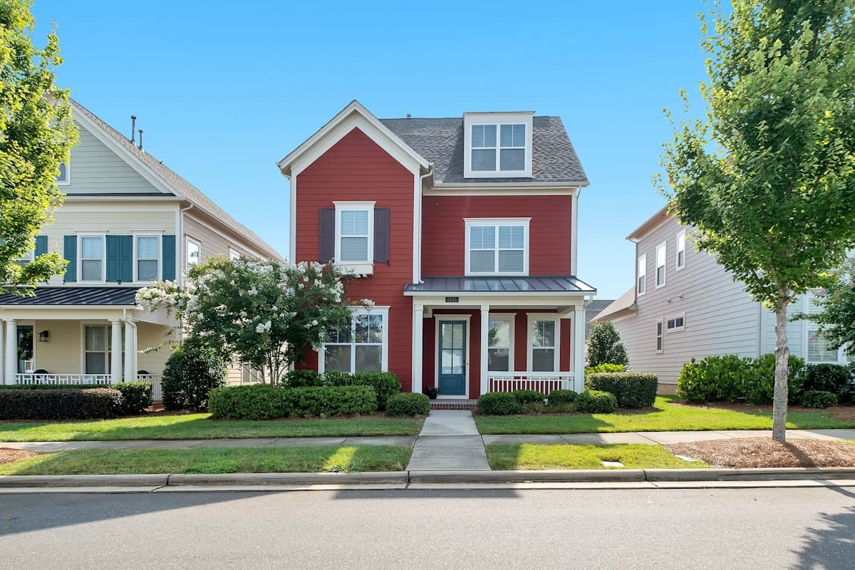 A red two-story home on a sunny suburban street