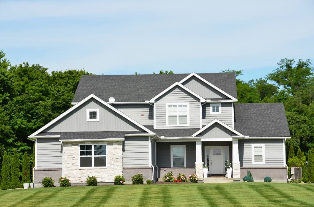 A two-story suburban home with gray siding, a green lawn, and a blue sky